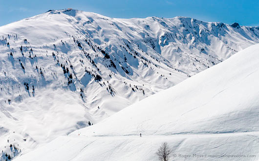 Skier on mountainside beside snow-covered valley above Saint Colomban, Les Sybelles, French Alps