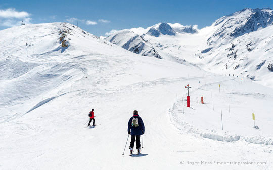 Skiers on wide open piste among snow-capped mountains, La Toussuire, French Alps