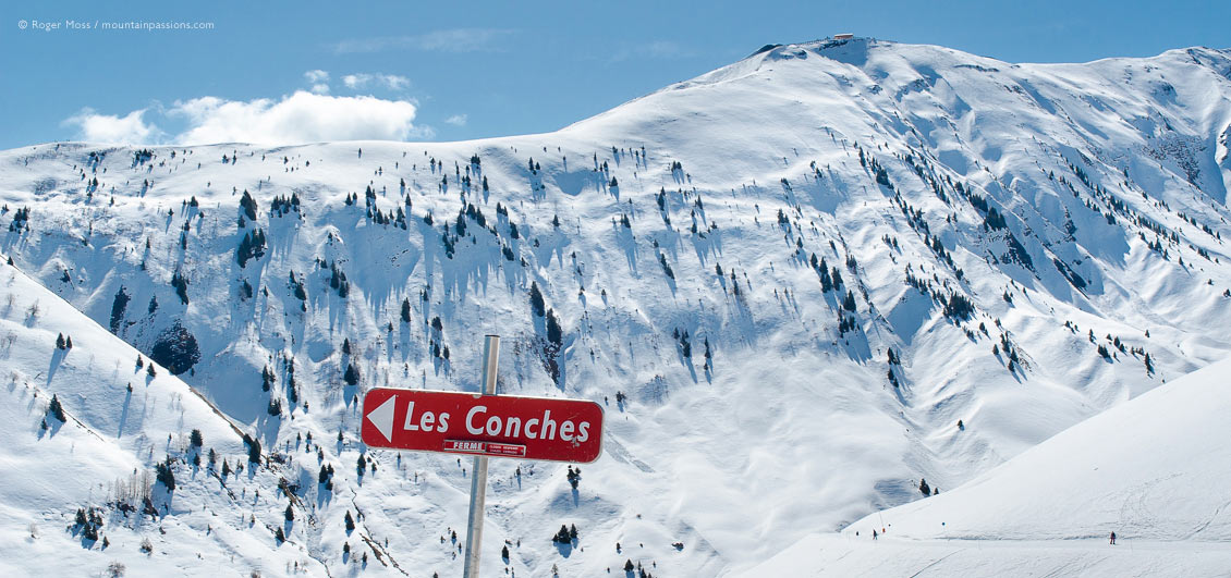 View past ski piste sign to mountainside with skiers at La Toussuire.