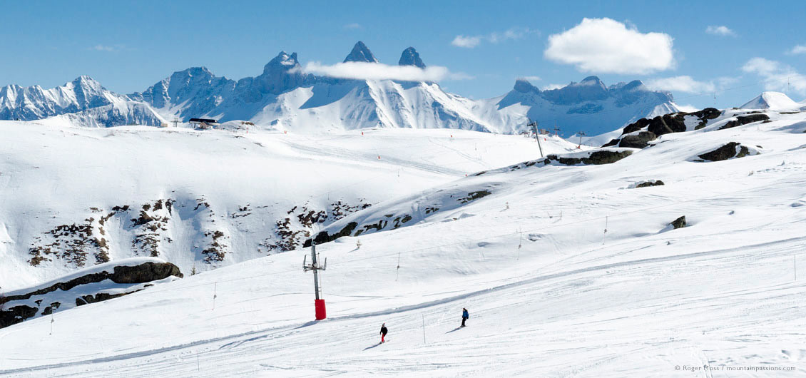 Long view of skiers on wide piste with distant peaks at La Toussuire, Les Sybelles, Maurienne, French Alps.