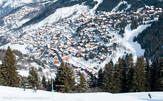 Skiers on steep piste high above ski village set among trees