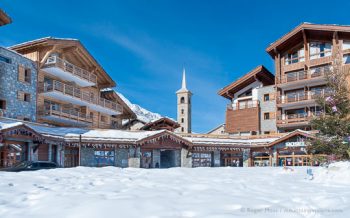 View across fresh snow to chalet-style ski village, with church spire in background