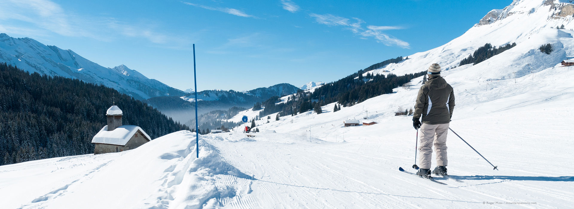 Low, wide view of skier in piste approaching mountain chapel