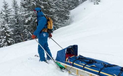 Rear view of ski security patrol skiing with recovery sled during snowfall