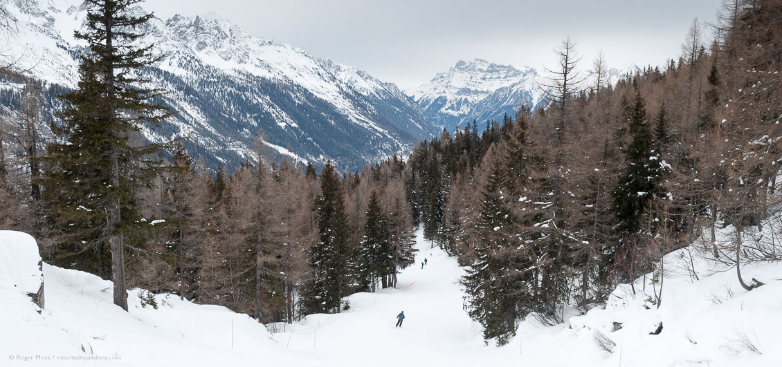 Wide view down ski piste, with forest and mountains above Vallorcine