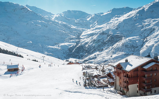 High view of snow-covered valley with mountain restaurant, ski apartments and skiers at Les Menuires