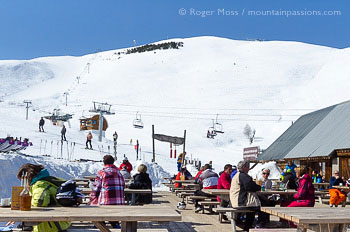 Skiers relaxing on sun terrace above Les 2 Alpes, with mountainside and chairlift