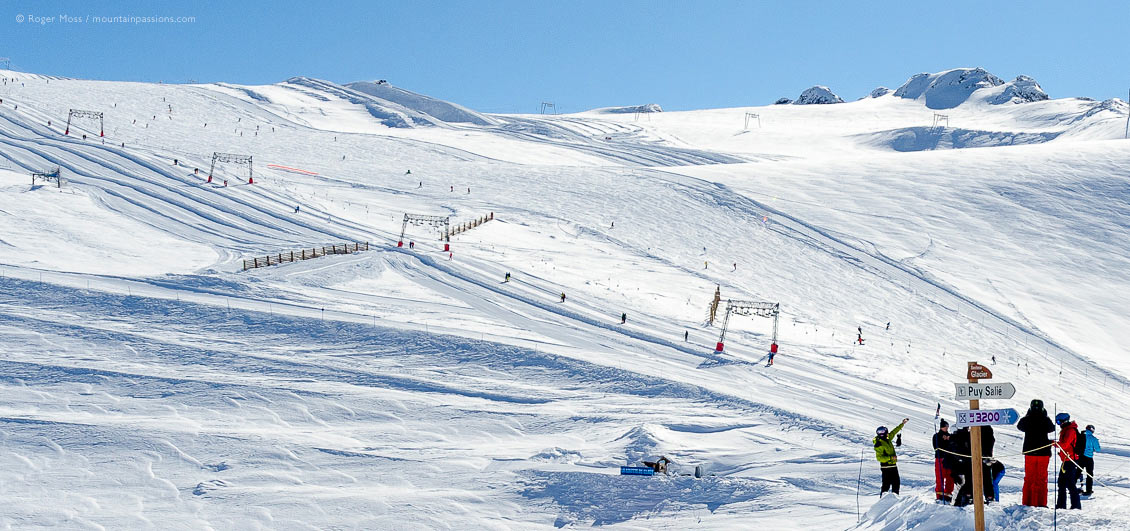 Long view of skiers at base of snow-covered glacier with ski-lift