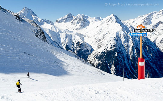 Skiers on steep piste, passing signage at Les 2 Alpes