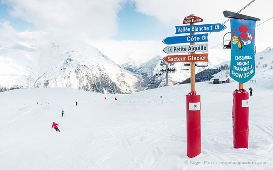 Wide view of mountainside with skiers passing signage at Les 2 Alpes