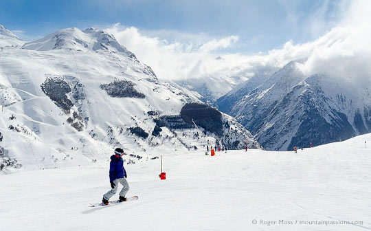 Wide view of snowboarder with valley, ski village and mountains at Les 2 Alpes