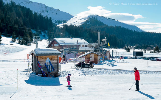 Young child on skis with father near ski lifts at Sommand, French Alps.