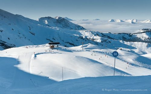 Wide overview of skiers, pistes and ski lifts above Chatel, Portes du Soleil, French Alps.