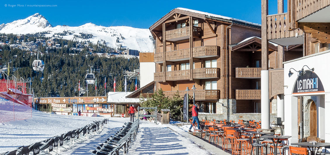 View of front-de-neige cafe terrace and gondola ski lift at Courchevel Moriond, French Alps.