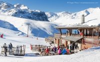 View of mountain restaurant, with skiers and snow-covered mountains above Courchevel Moriond, French Alps.