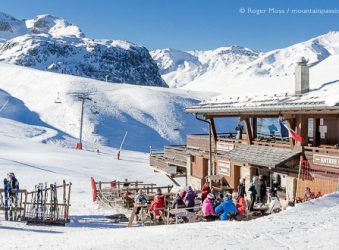 View of mountain restaurant, with skiers and snow-covered mountains above Courchevel Moriond, French Alps.