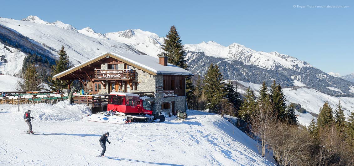 Two skiers passing mountain restaurant at Valmorel, Savoie, French Alps.