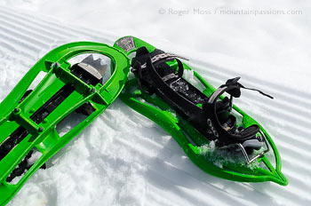 Pair of lightweight showshoes on snow, showing piste grooming lines.