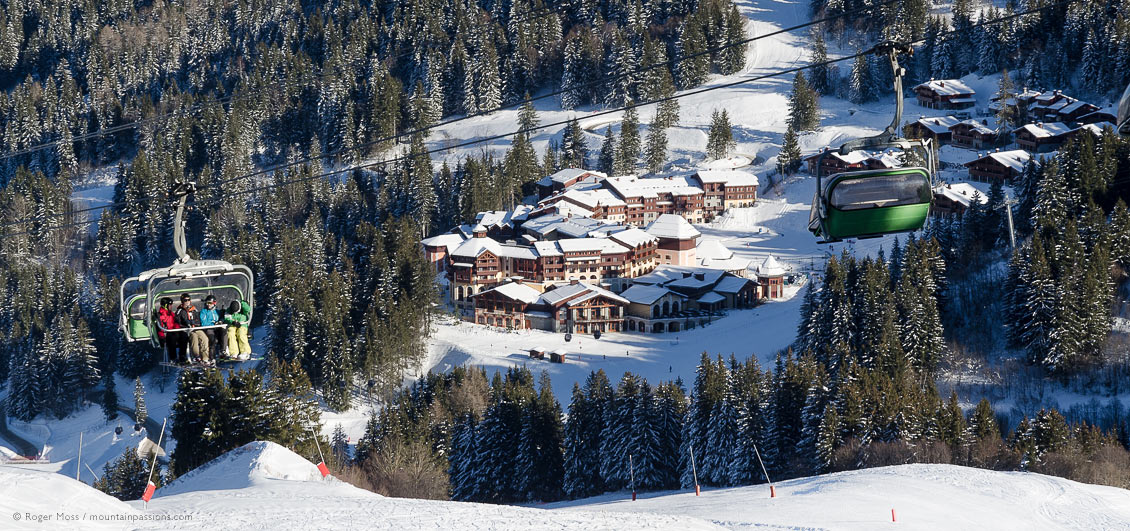 Skiers on chairlift above Club Med village set among trees at Valmorel, French Alps.