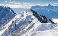 Wide overview of skiers on piste with big mountain views at Praz de Lys