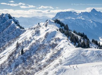 Wide overview of skiers on piste with big mountain views at Praz de Lys