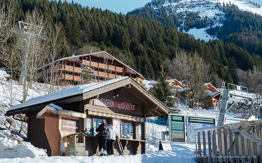 Skiers buying lift passes beside chair-lift, with chalets and mountainside