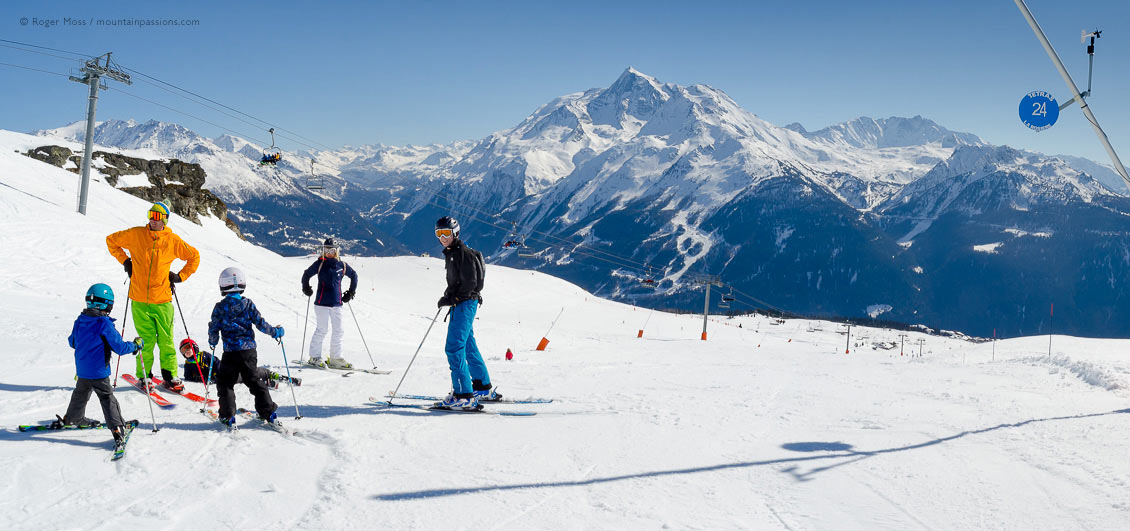 Wide view of family skers beside piste with chairlift and mountains at La Rosiere